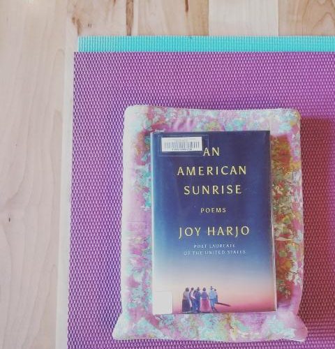 Image Of An American Sunrise: Poems By Joy Harjo On A Pink, Yellow, Turquoise Book Sleeve On A Purple And Turquoise Yoga Mat On A Wood Floor