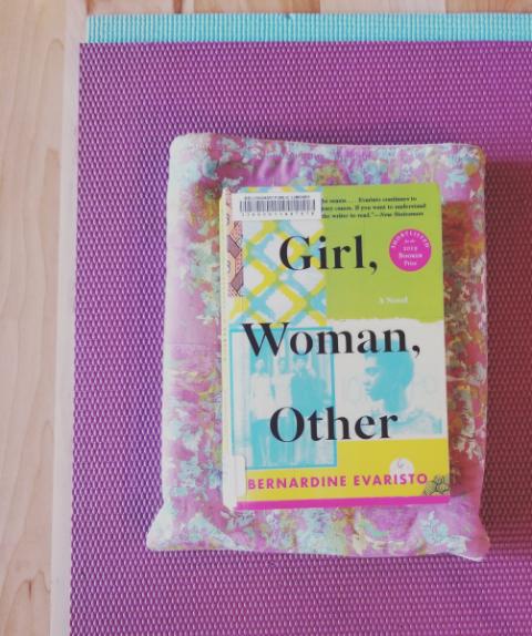 Photo of the book Girl, Woman, Other by Bernardinef Evaristo on a light purple yoga mat on wood flooring
